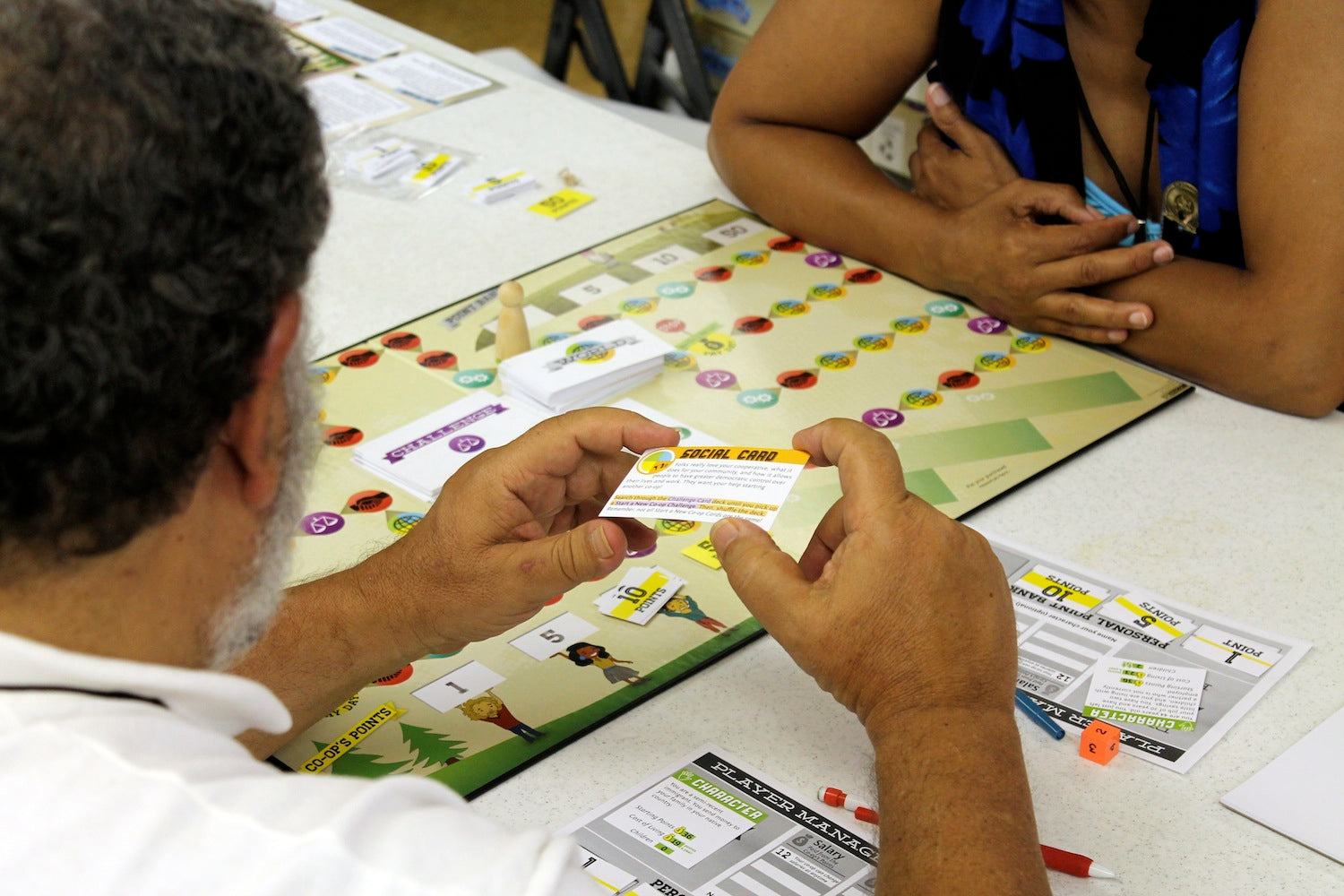 Two people playing a board game with cards on a table.